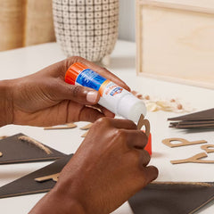Hands using Elmer's disappearing glue stick to apply glue to paper craft pieces