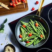 Black speckled non-stick fry pan with gold handle, filled with green beans.