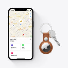 Apple AirTag tracker with brown leather key fob and keys beside an iPhone screen