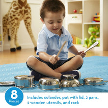 Boy playing with stainless pots and pans on a blue mat