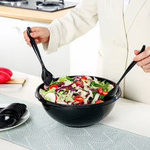 Two black plastic serving spoons serving salad from a large bowl