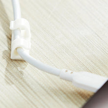 Single white adhesive cable management clip securing a cable on a light wood surface.