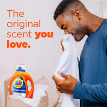 Orange liquid laundry detergent bottle beside folded white shirts, with a person holding fabric.