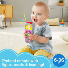 Baby holding a gray learning remote toy with multicolor buttons and a red top