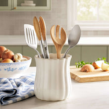 White stoneware utensil holder holding wooden and metal kitchen utensils