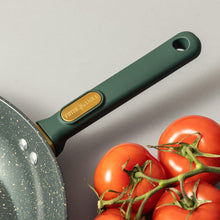 Speckled nonstick skillet edge with dark green handle and gold emblem, with tomatoes