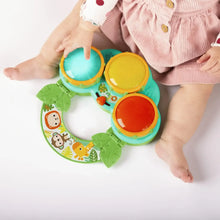 Infant holding a green musical drum toy with orange, yellow, and blue drum pads
