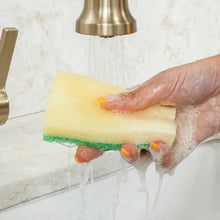 Dual-sided scrub sponge held in hand, yellow top and green scrubbing layer