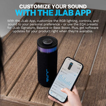 Black portable speaker with RGB top ring, textured fabric, and blue logo on a wooden deck.