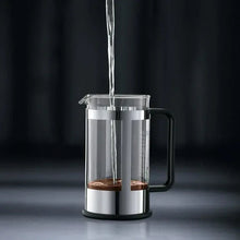 Stainless steel French press with coffee being poured into the glass chamber