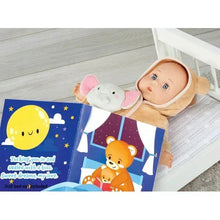 Baby doll in tan hooded sleeper beside a toy bed with blue animal bedding.