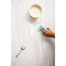 Dual-sided scrub sponge on wet countertop with foam, held in a hand