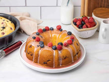 Gray fluted bundt cake pan next to decorated cake on a serving plate.