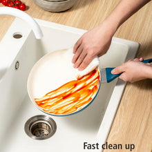 Blue ceramic nonstick skillet being wiped clean after cooking, near a sink drain