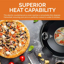 Electric countertop pizza oven in black beside a finished pizza on a stone surface.