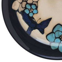 Stoneware plate detail with navy butterfly, teal flower clusters, and dark rim