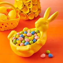Yellow hand-shaped bowl filled with multicolored candy eggs and pieces, with bunny