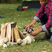 Man holding a propane cylinder while lighting a campfire outdoors