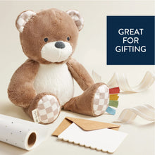 Plush bear sitting with checkered paws and multicolor ribbon sensory tags