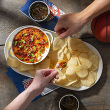 Potato chips on a serving plate with salsa bowls and hands holding chips
