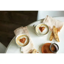 Coffee mugs with foam tops, dark coffee, and bread pieces on a tray