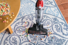 Stick vacuum nozzle on a blue patterned rug with clear dust bin