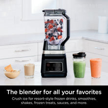 Black blender with clear jar filled with berries and ice, plus smoothie cups