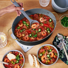 Black multi-cooker pot with shrimp and peppers, serving ladle and bowls
