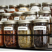 Clear spice jars with metal lids with visible herb labels like thyme and rosemary