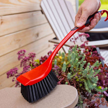 Red scrub brush with black bristles held for cleaning a deck corner