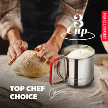Stainless steel flour sifter with red handle on countertop