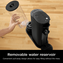 Black pod coffee brewer with removable reservoir and jug pouring into the brew chamber.