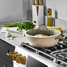 Taupe sauté pan on gas stovetop with lid open and gold handles