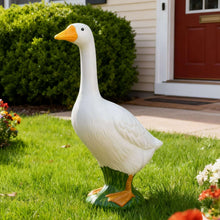 White goose yard statue with yellow beak and green feet on grass.