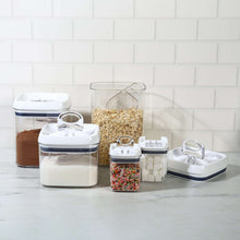 Clear food storage containers with flip lids, holding dry baking ingredients on a counter