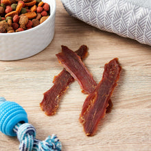 Duck jerky dog treats, dark red strips and chips on a wooden surface