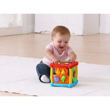 Infant playing with a colorful plastic activity cube toy with orange and red face buttons