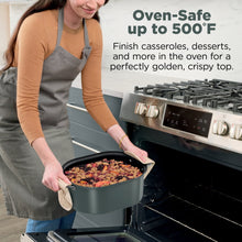 Sage green multi-cooker pot being placed into an oven, hand on handle