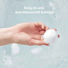 Hand holding a white vapor bath bomb over foamy water