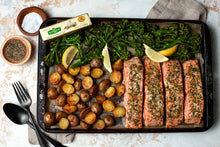 Garlic and herb butter stick shown near roasted meat, asparagus, and herb leaves