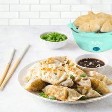 Teal egg cooker with open lid beside plated steamed omelet with sauce and herbs