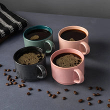 Set of 4 stoneware coffee mugs in teal, black, and blush pink, filled with coffee