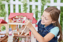 Children playing with dollhouse playset, red-roof home with open balcony and rooms