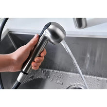 Hand holding brushed nickel pull-out spray head delivering a steady stream.