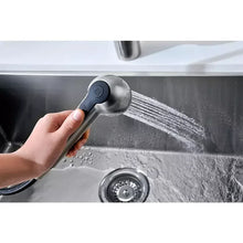 Hand using brushed nickel pull-out spray head with soft spray pattern.