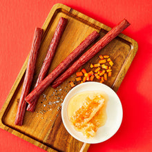Hot honey beef sticks on a wooden board with sliced pieces and a small sauce bowl