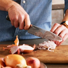 Knife with stainless Damascus blade and dark wood handle chopping onions on wooden board