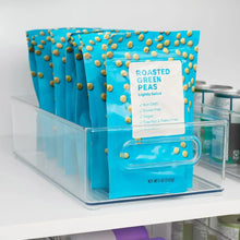 Clear kitchen bin holding multiple bags of roasted green peas, with a front divider