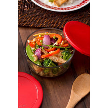 Glass food storage container with red lid, filled with salad and vegetables