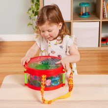 Child placing a red toy drum on a table with hanging strap